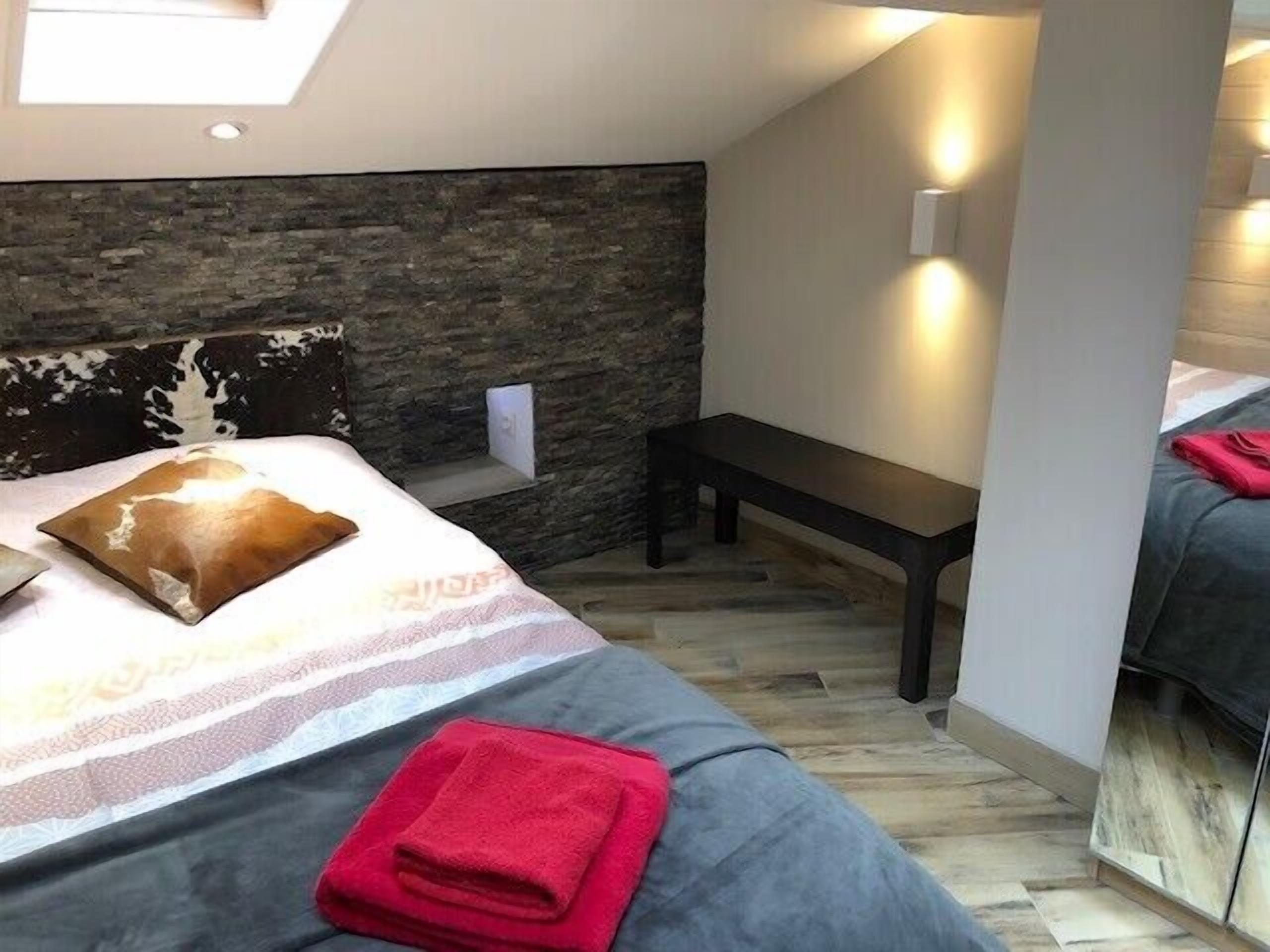 A modern bedroom with a stone accent wall, a bench, and a skylight.