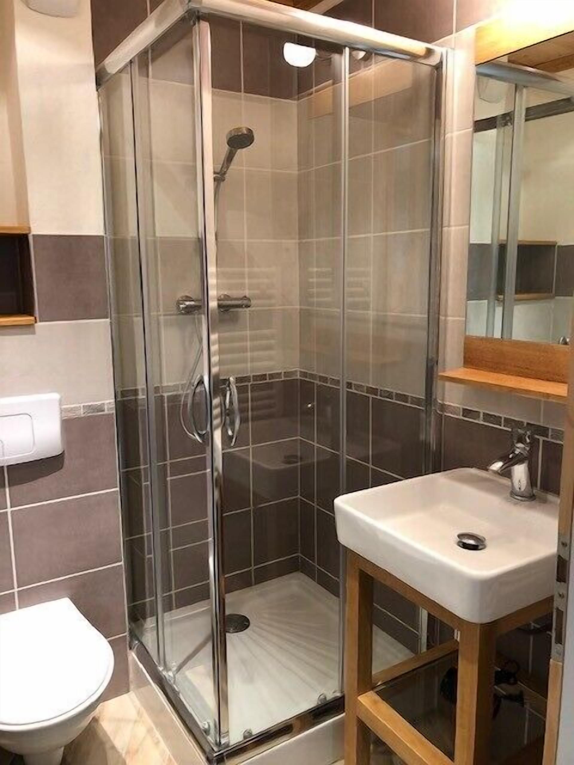 A modern bathroom with a glass-enclosed shower, a white sink, and a wooden vanity.