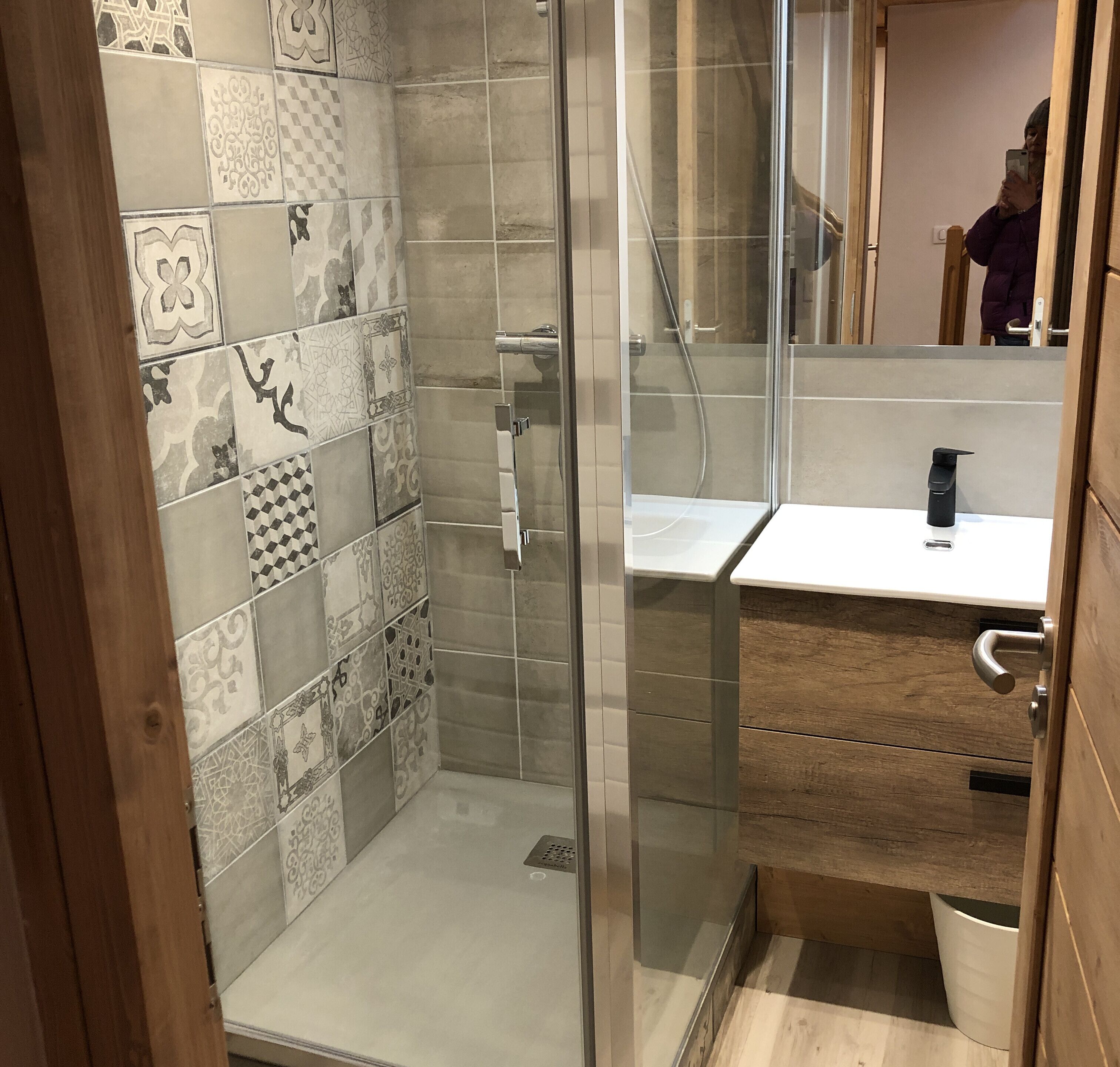 Un espace douche doté d’une porte en verre, de murs carrelés et d’un meuble-lavabo en bois avec un évier.