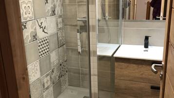 Un espace douche doté d’une porte en verre, de murs carrelés et d’un meuble-lavabo en bois avec un évier.