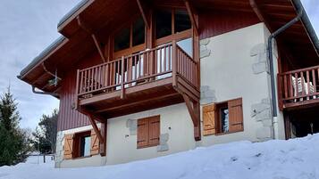 Un bâtiment de style chalet, doté d’un balcon en bois, de murs en pierre et d’un sol recouvert de neige.
