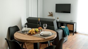 Un comedor moderno con una mesa redonda, sillas negras y suelo de madera. Un televisor de pantalla plana está montado en la pared sobre la zona de estar.