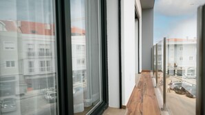 Un pasillo con amplios ventanales, piso de madera y vista a una calle con coches aparcados.