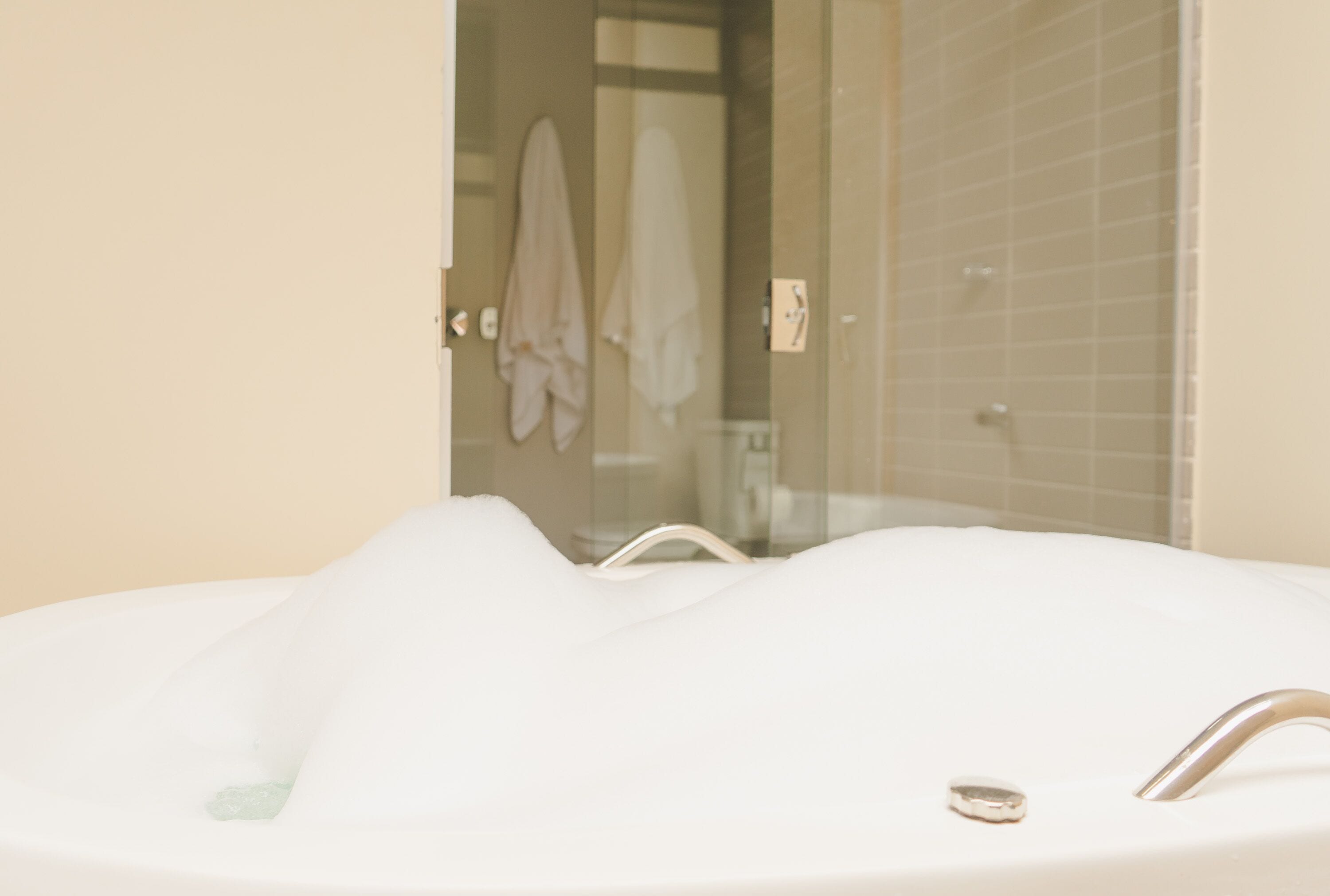 A bathroom with a bathtub filled with bubbles, a glass shower enclosure, and a towel rack with towels.