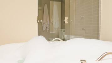 A bathroom with a bathtub filled with bubbles, a glass shower enclosure, and a towel rack with towels.