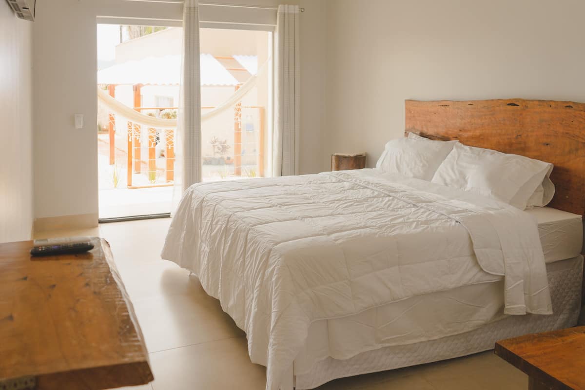 A bedroom with a large bed, a wooden headboard, a wooden nightstand, and a view of a balcony.