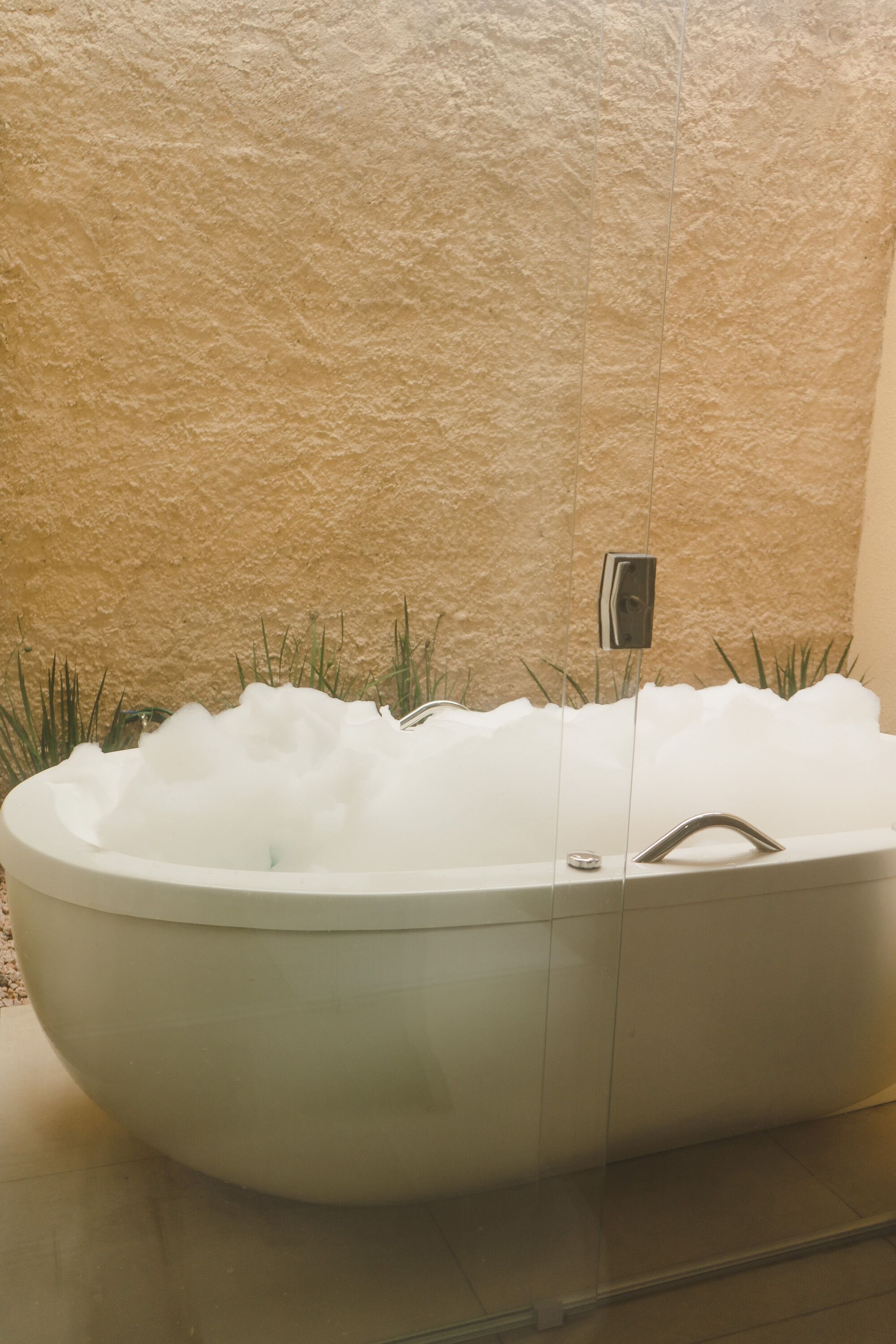 Un jacuzzi grande y ovalado, lleno de agua, ubicado frente a una pared con textura.
