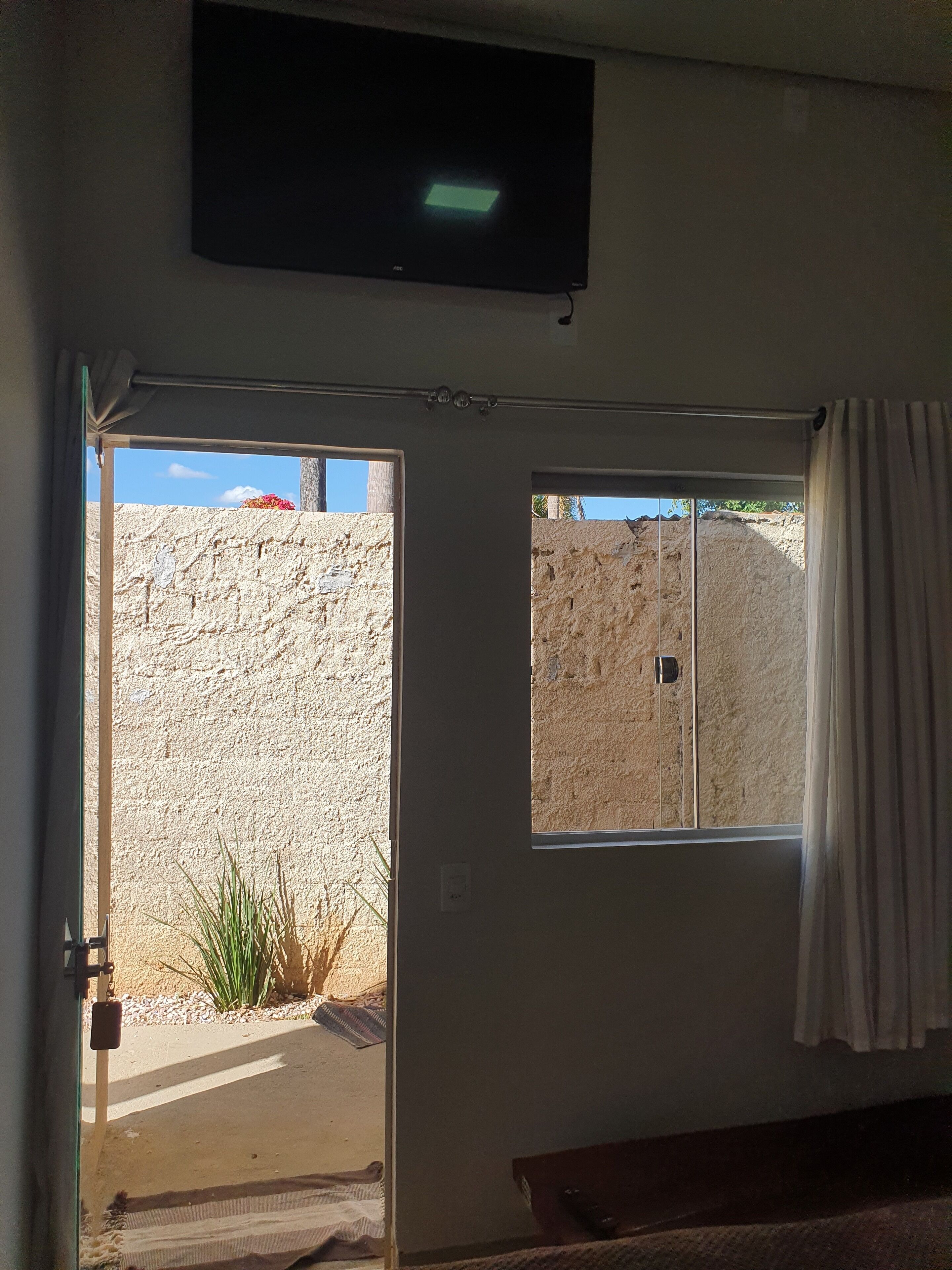 A room with a television mounted on the wall, a door leading outside, and a window with curtains.