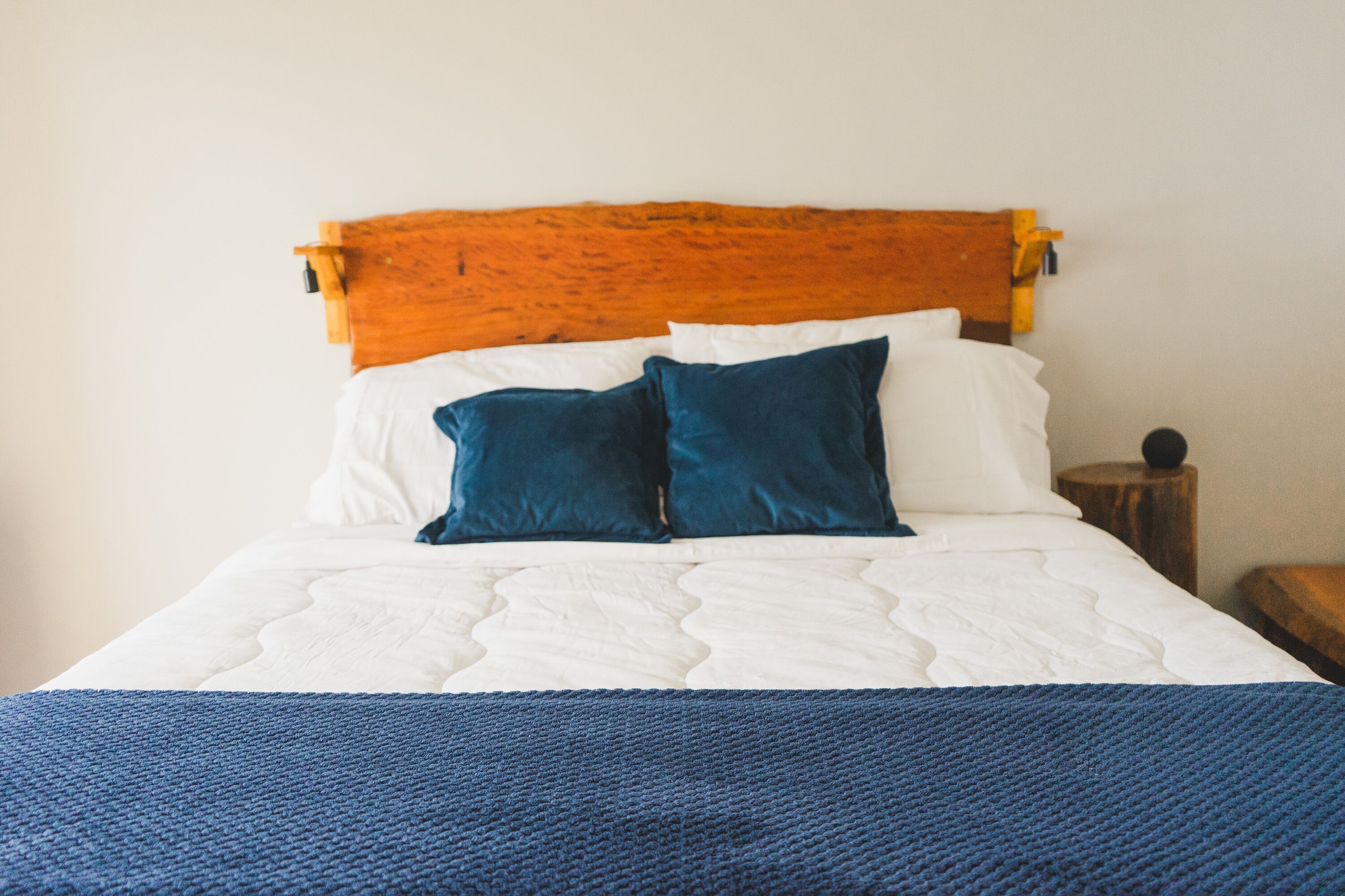 A bed with a wooden headboard, white bedding, and two blue pillows.