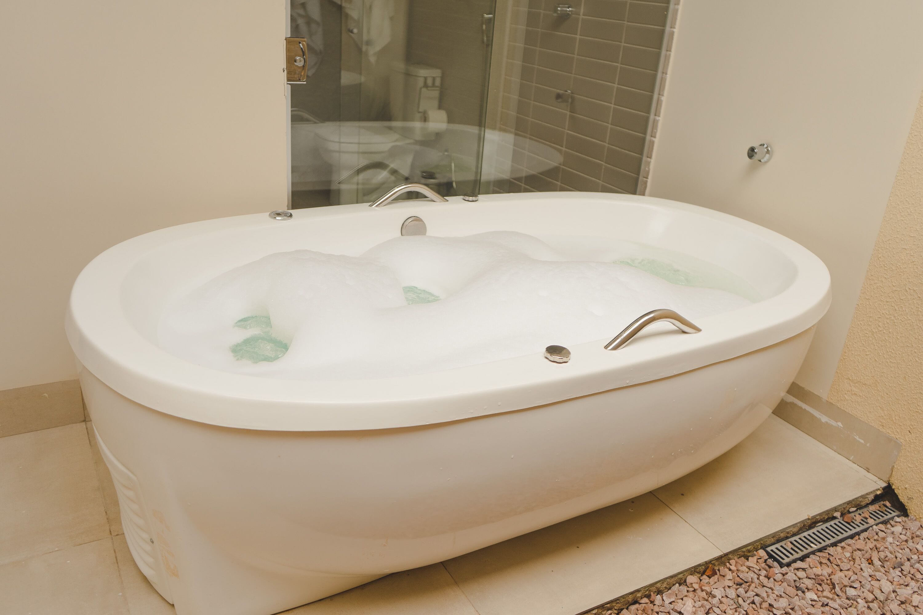 A large, freestanding bathtub in a bathroom with a glass shower enclosure and a tiled floor.