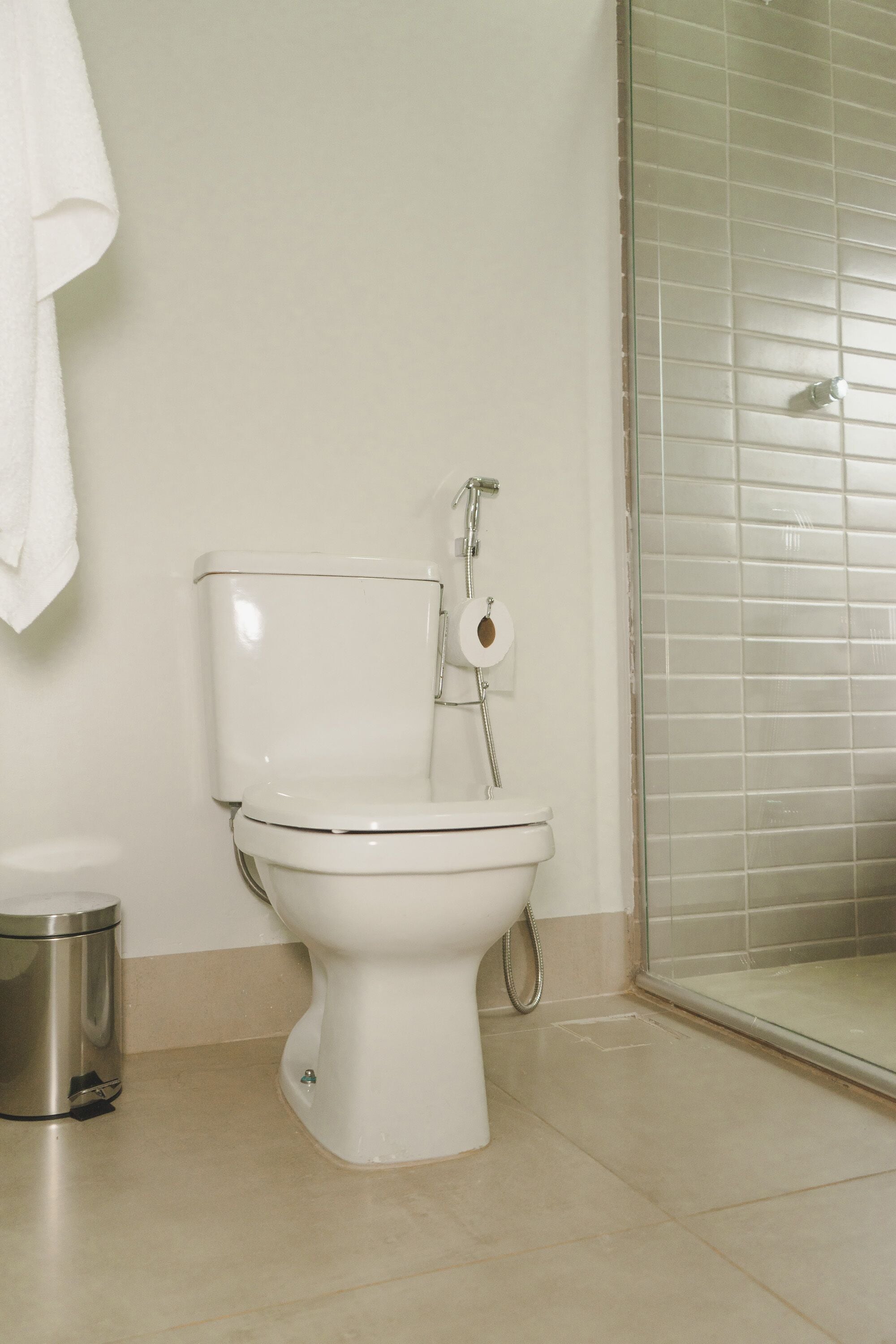 Des toilettes blanches avec un porte-serviettes en papier, une poubelle et un espace douche doté d’une porte en verre.