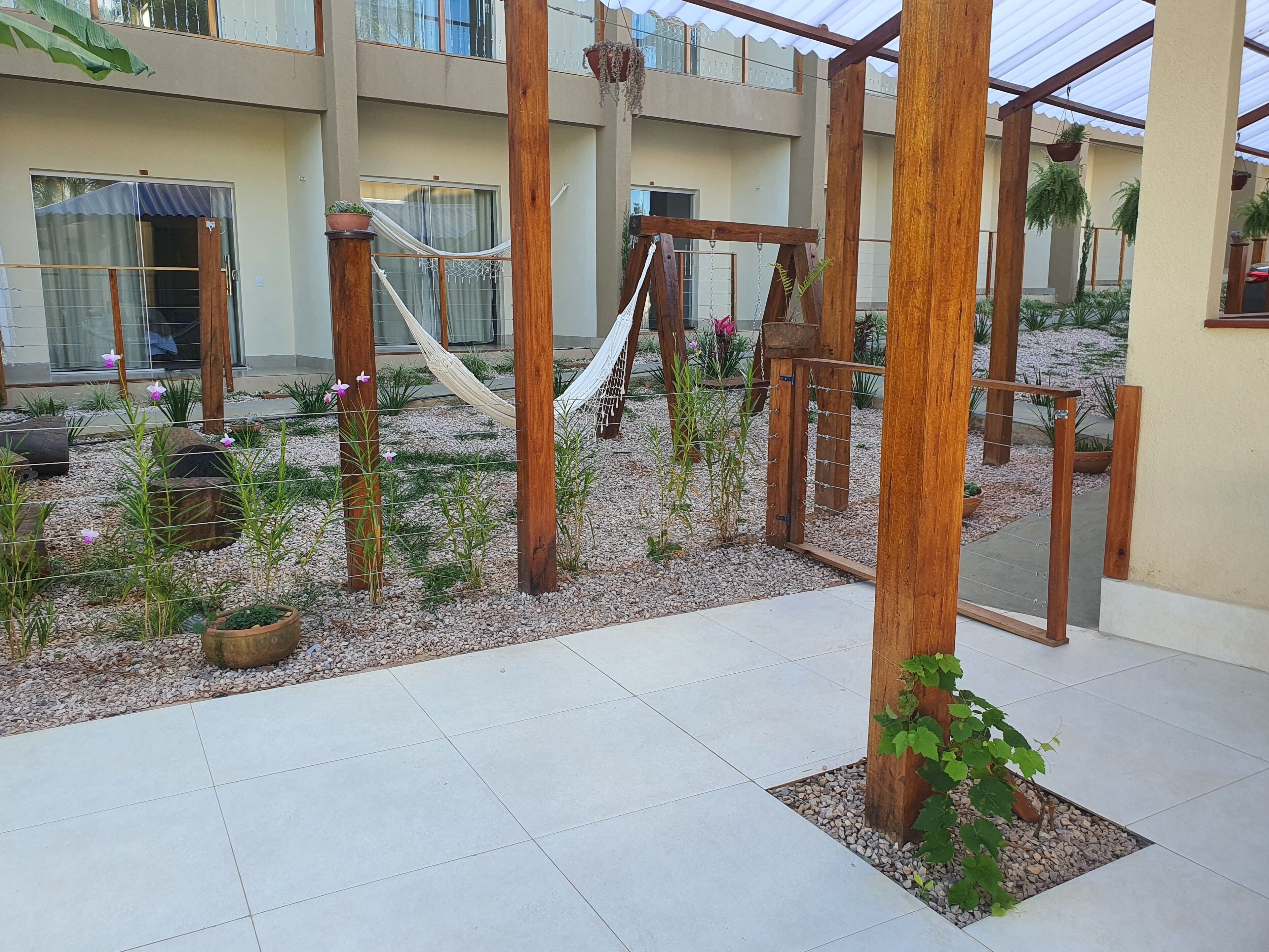A modern outdoor area with a hammock, wooden play structures, and a garden with various plants and flowers.