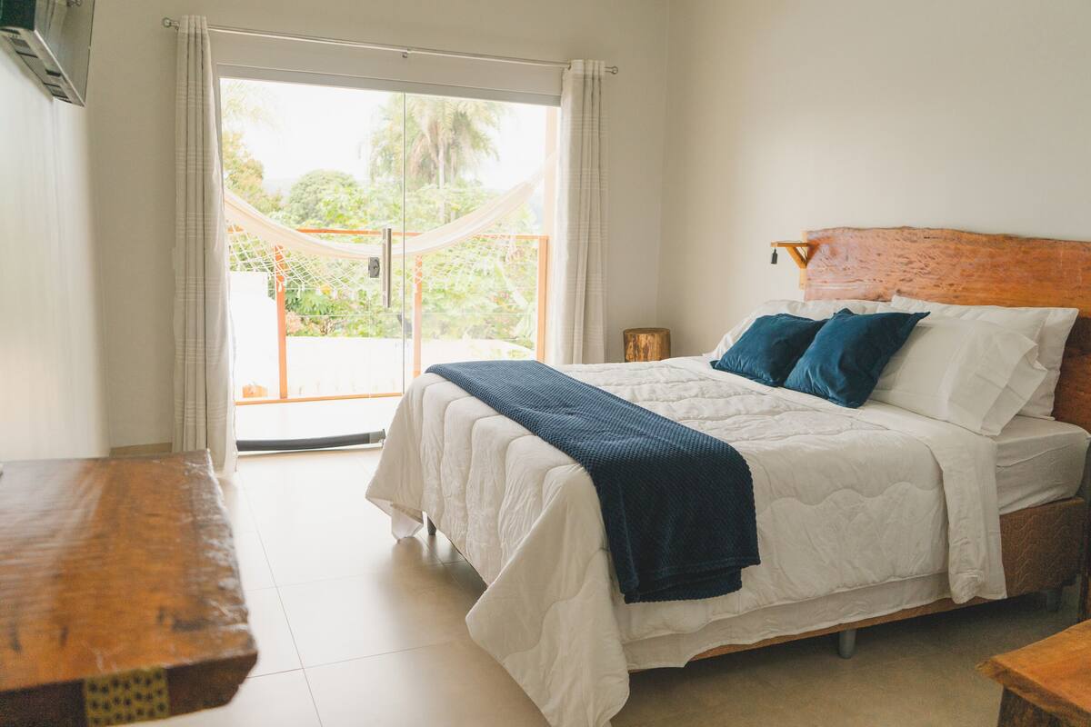 A bedroom with a bed, a wooden headboard, a nightstand, and a view of a balcony with a net.