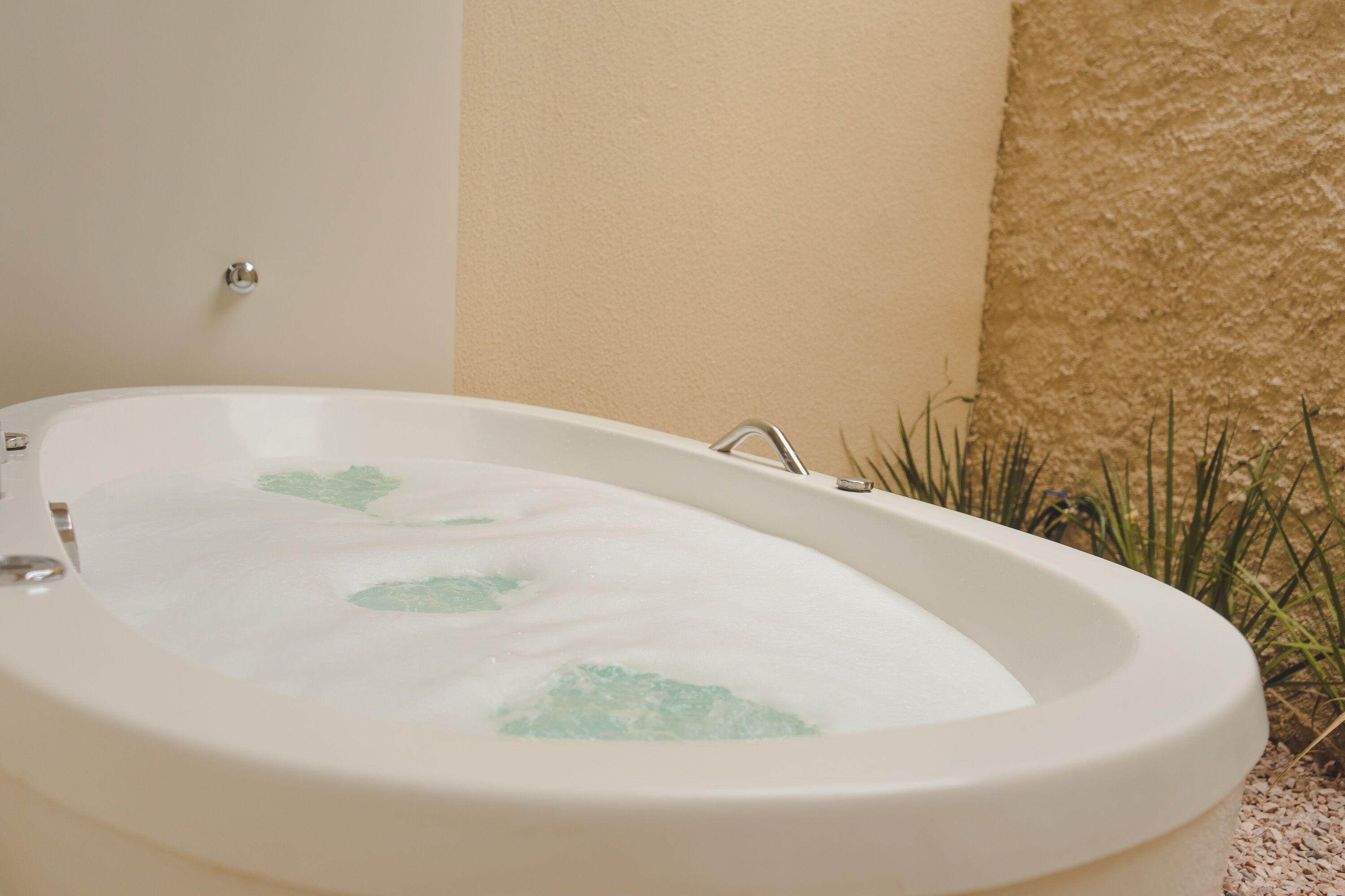 A white bathtub with green leaf patterns, a wall-mounted faucet, and a textured wall beside it.