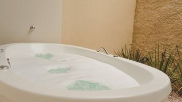 A white bathtub with green leaf patterns, a wall-mounted faucet, and a textured wall beside it.