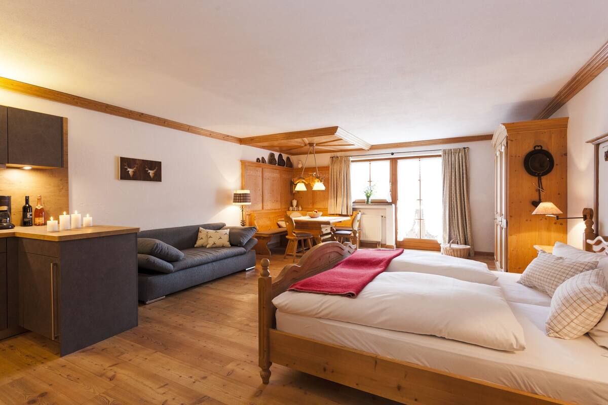 A cozy room with a bed, a sofa, a dining table, and a kitchen area.