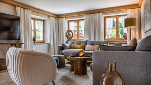 A cozy living room with a sofa, armchair, and coffee table. There is a TV mounted on the wall and a lamp on a side table. - Fiakerhof (Garmisch-Partenkirchen)