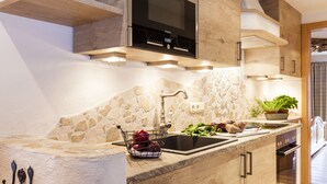 A modern kitchen with a stone backsplash, a built-in microwave, and a sink. - Fiakerhof (Garmisch-Partenkirchen)