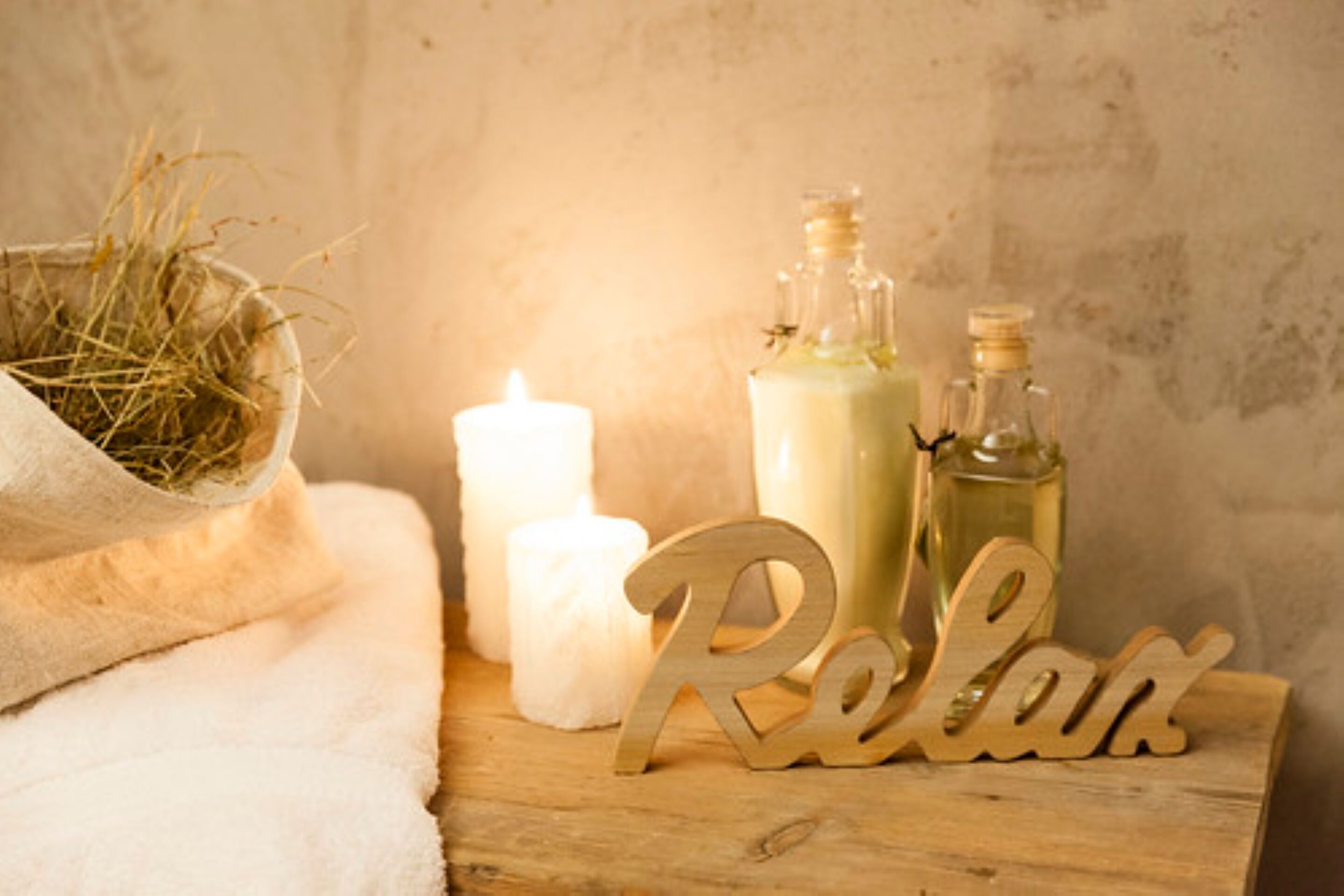 A wooden table with a white candle, two bottles of liquid, and a 'Relax' sign.