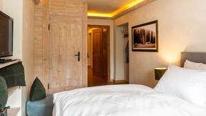 A hotel room with a wooden wardrobe, a bed with white bedding, a television on a stand, and a framed picture on the wall. - Fiakerhof (Garmisch-Partenkirchen)