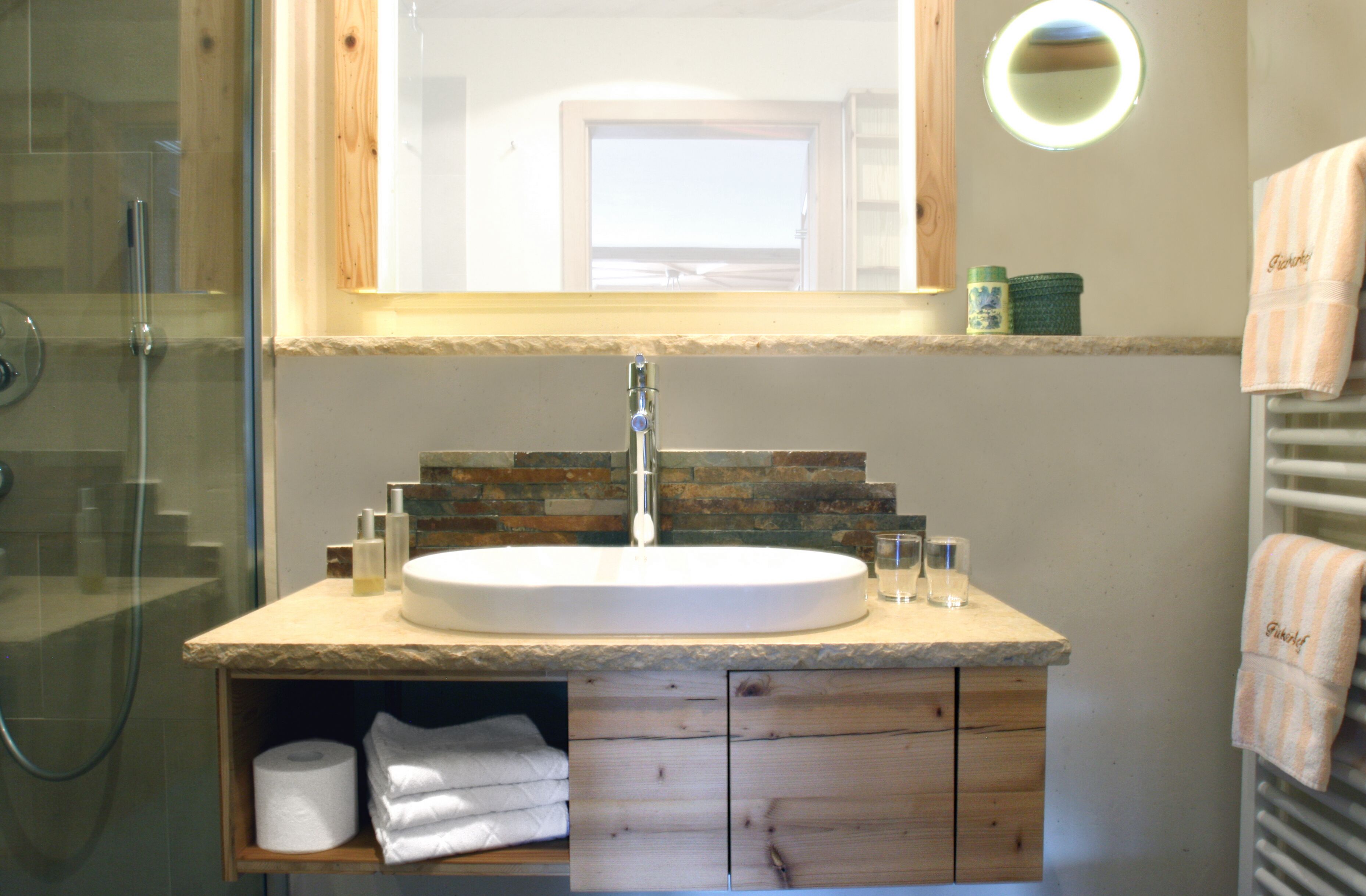 Un baño con tocador de madera, lavamanos blanco y cabina de ducha de vidrio.