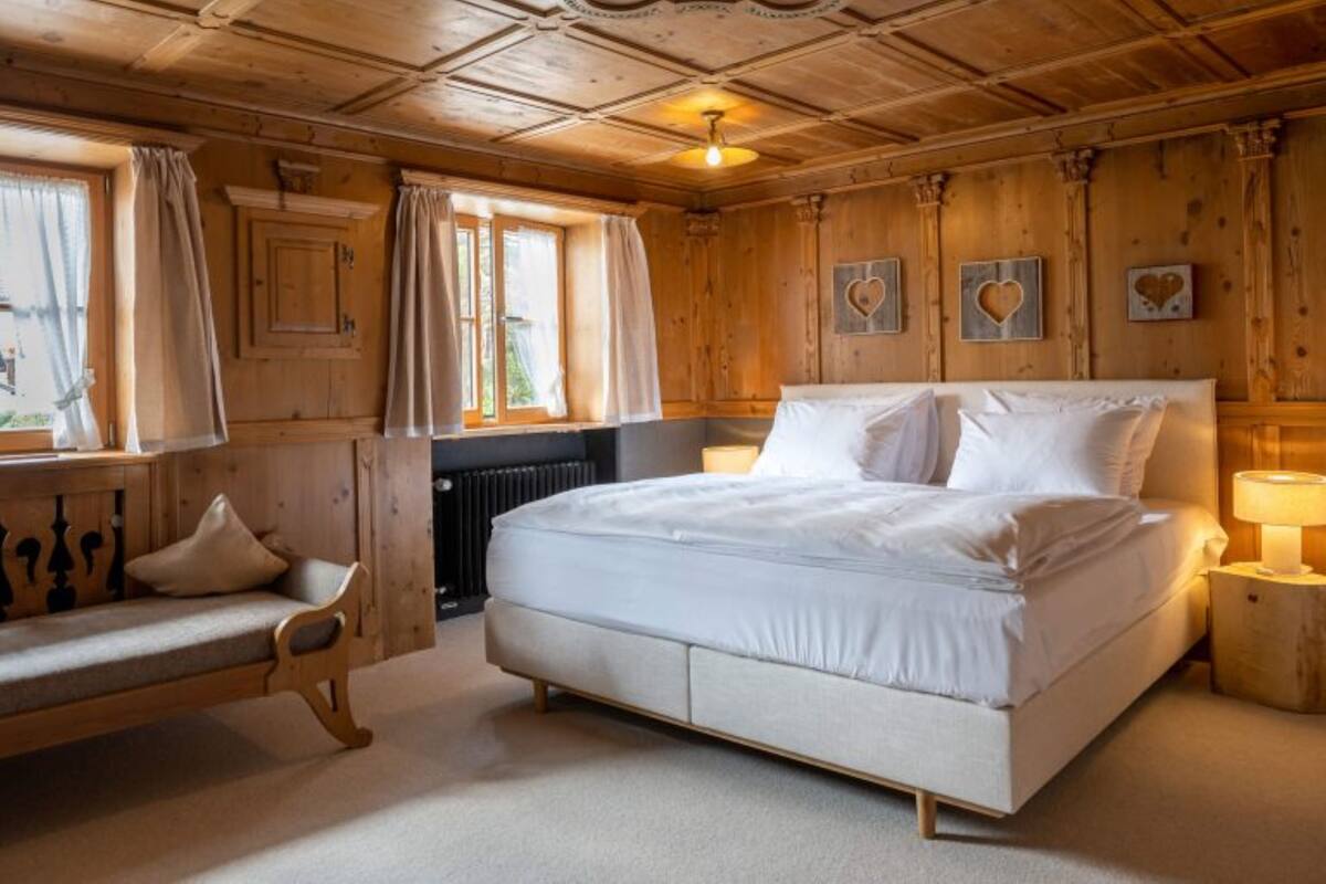 A bedroom with a large bed, a wooden bench, and a window with curtains.