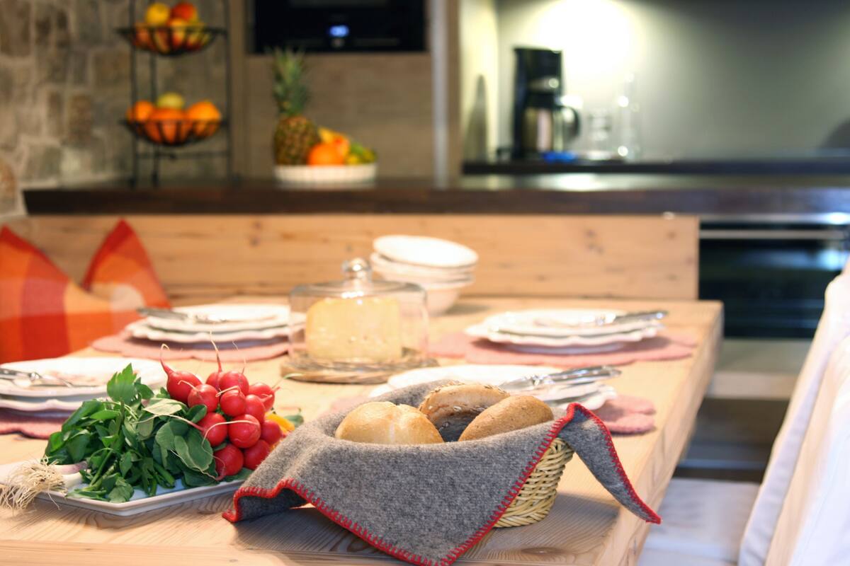 A dining table set with plates, a basket of bread, and a glass container of cheese.
