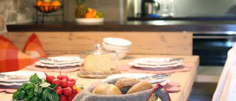 A dining table set with plates, a basket of bread, and a glass container of cheese.