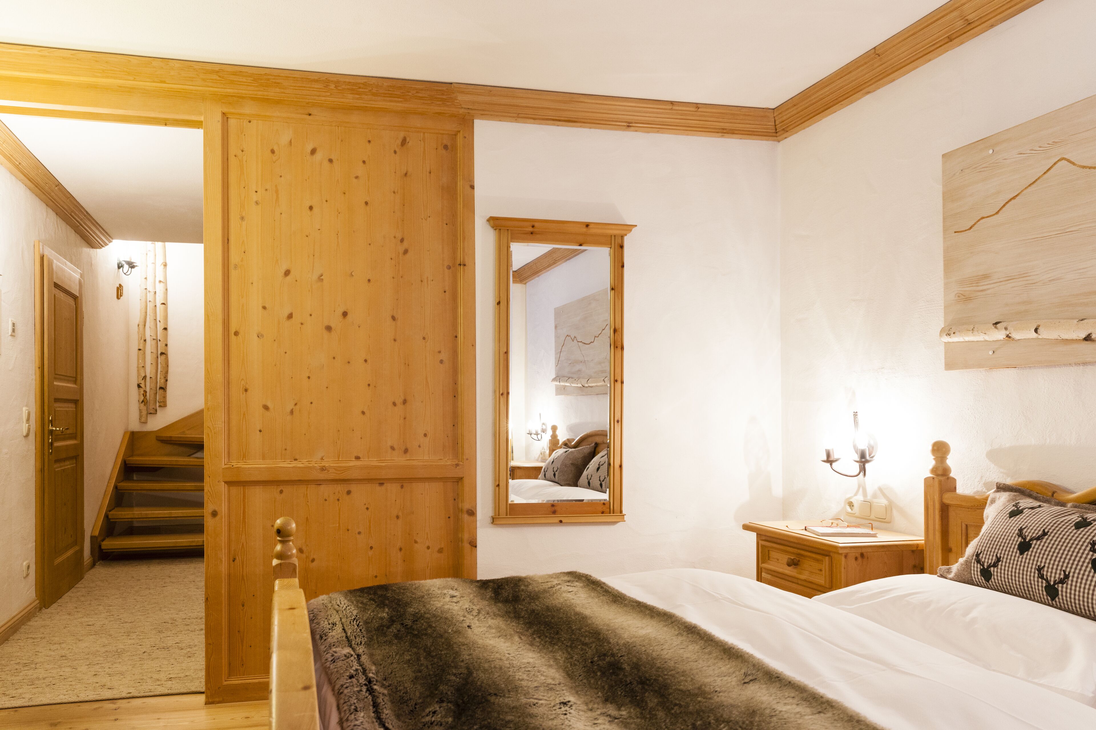 Un dormitorio con cabecero de madera, una mesita de noche con lámpara, un espejo y una escalera que lleva a otra habitación.