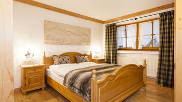 A wooden bed with a headboard, a bedside table with a lamp, a wall-mounted artwork, and a window with curtains.