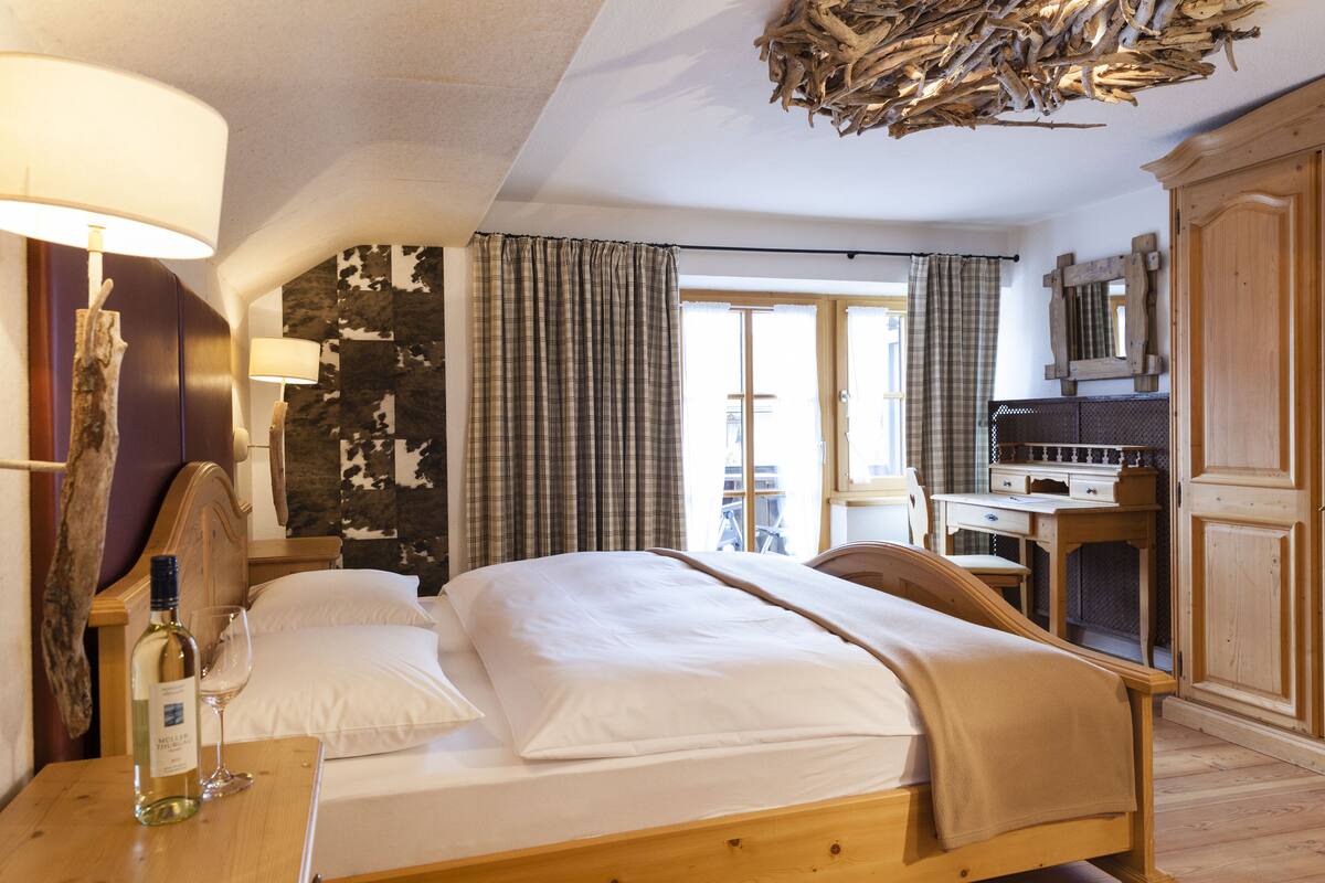 A hotel room with a bed, a desk, a chair, a lamp, and a bottle of wine.