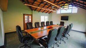 Una sala de conferencias con una larga mesa, varias sillas, un ventilador de techo y un televisor en la pared.