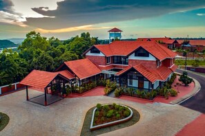 A modern building with multiple red-roofed structures, surrounded by greenery and a landscaped area with a heart-shaped garden. - Vaidekam Resort and Ayurveda Healing Village, Kannur (Talipparamba)