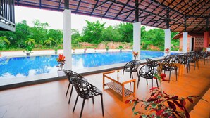 Zona de piscina cubierta con sillas y mesas, vista a la piscina y follaje circundante.