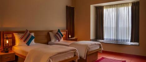 A hotel room with two beds, a red rug, a window with curtains, and a wall-mounted light fixture.