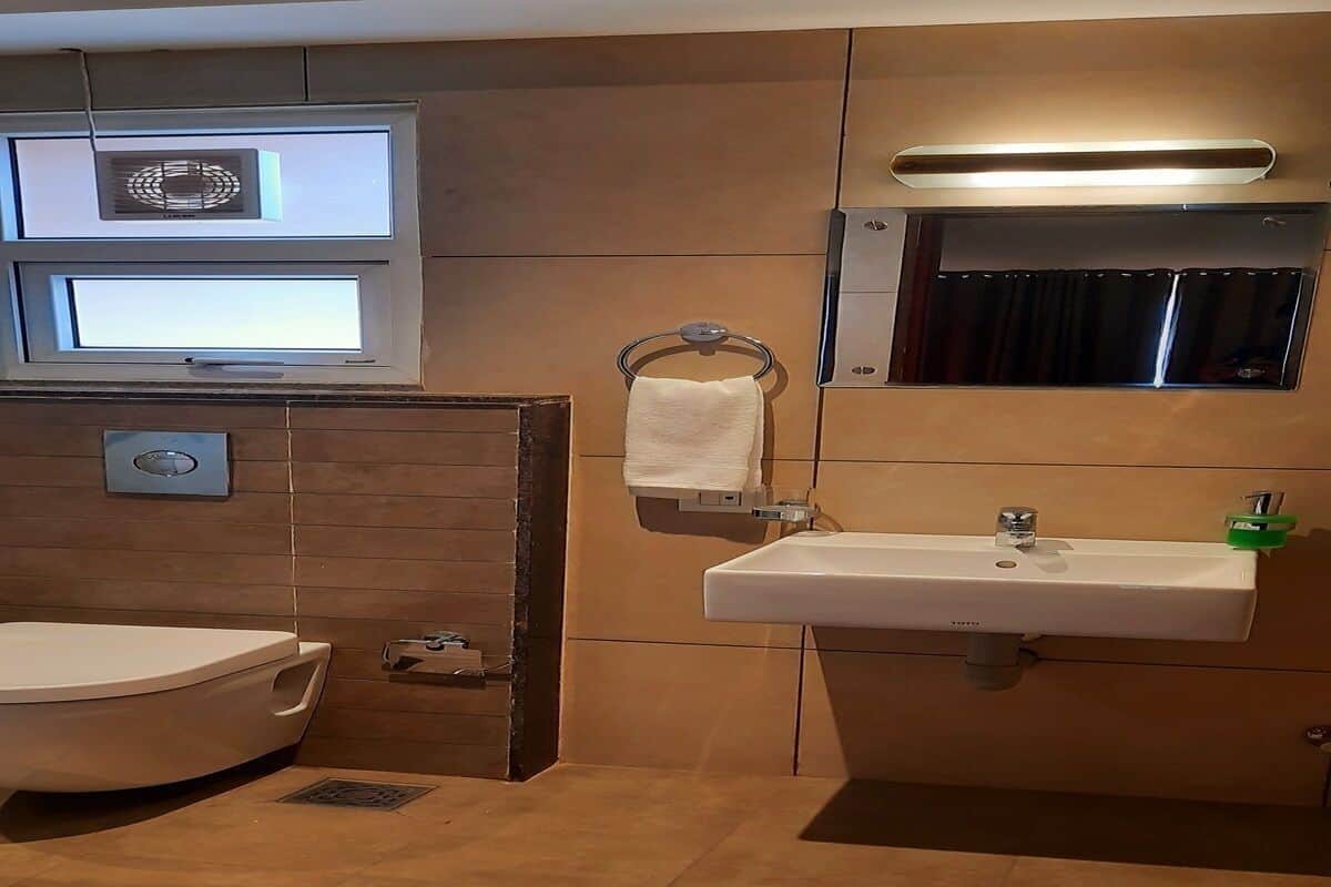 A bathroom with a toilet, sink, towel rack, and a window above the sink.
