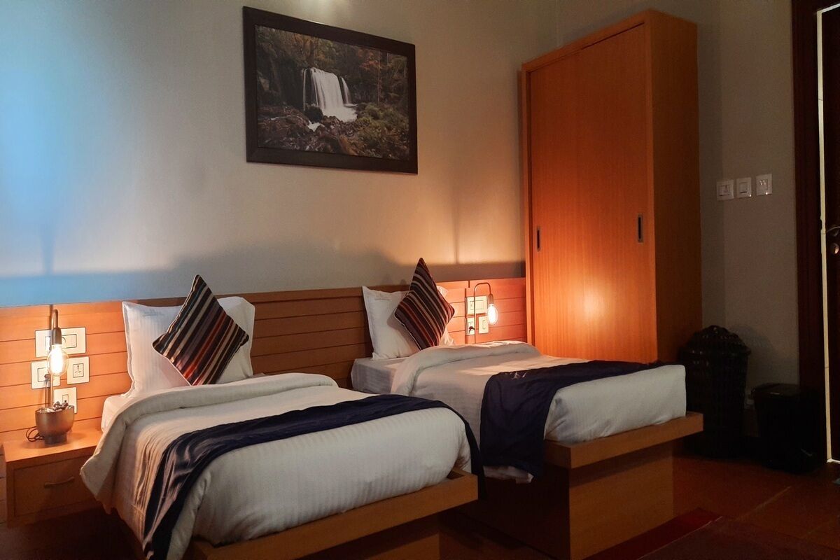 A hotel room with two beds, wooden headboards, a large wardrobe, and a wall-mounted picture of a waterfall.