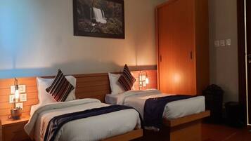 A hotel room with two beds, wooden headboards, a large wardrobe, and a wall-mounted picture of a waterfall.