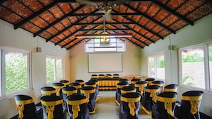 Un salón de conferencias con techo alto, hileras de sillas con cintas amarillas, una pantalla de proyector y amplias ventanas.