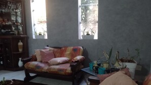 Un salon chaleureux avec un canapé, une table basse et une bibliothèque. De grandes fenêtres laissent entrer la lumière naturelle.