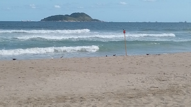 Une plage avec un rivage sablonneux, des vagues et une île qui se dessine à l’horizon.
