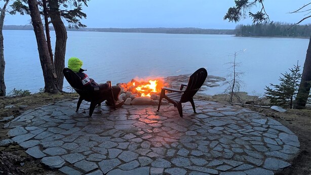 En eldstad av sten med två stolar och en person som bär en färgglad huvtröja.