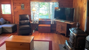 En mysig stuga med träpanel på väggarna, en fåtölj i läder, en soffa, en tv och en vedkamin.