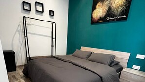Quarto moderno com cama, mesa de cabeceira, prateleira na parede e quadro com fogos de artifício.