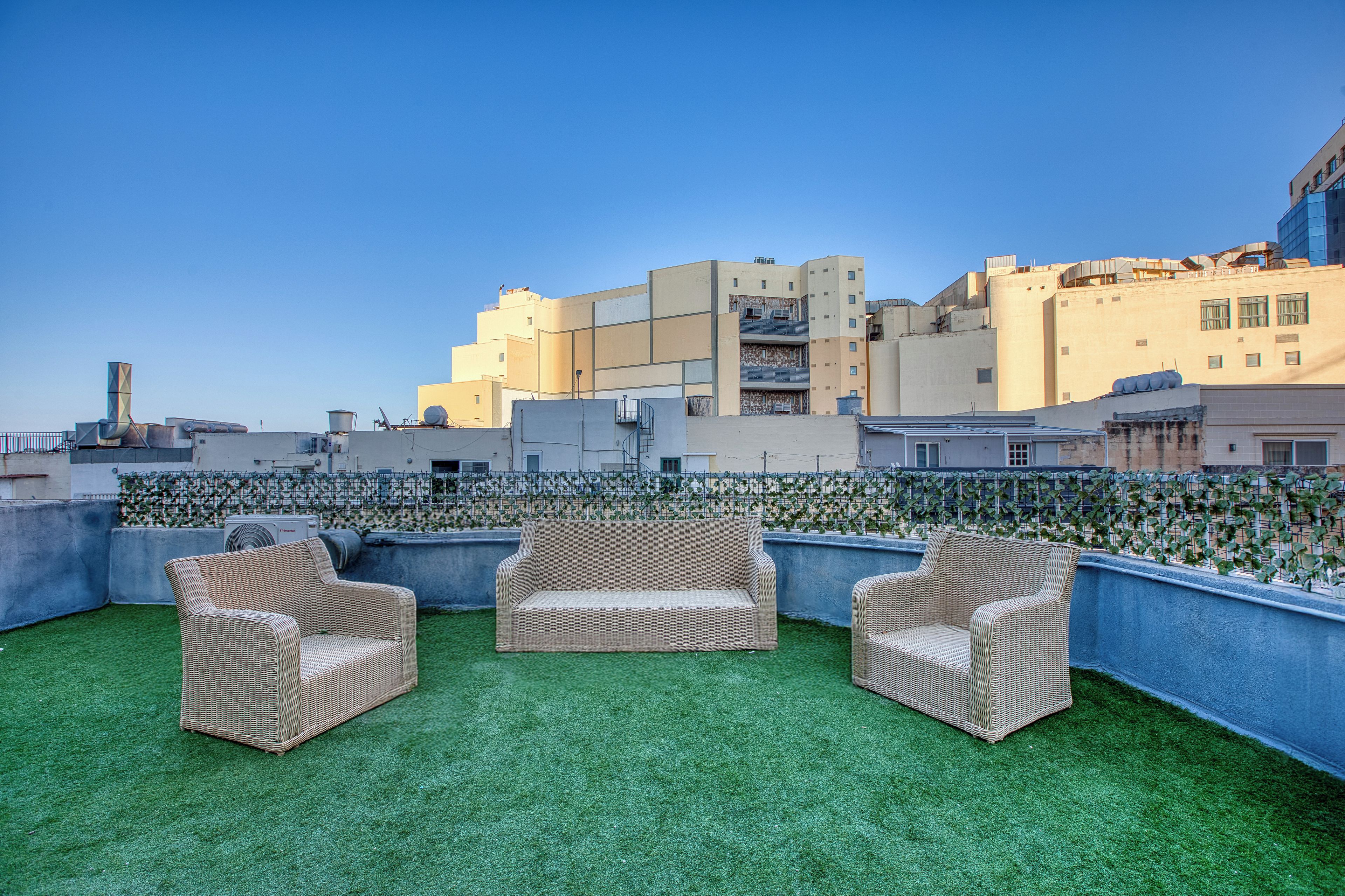Una terrazza panoramica sul tetto con prato artificiale, mobili in vimini e vista sugli edifici circostanti.