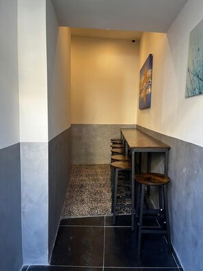 A narrow hallway with a dark tiled floor, a wooden table with four stools, and a painting on the wall. - Bookarest Hostel Malta (St. Julian's)
