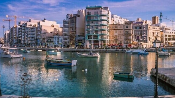 Uma marina com vários barcos atracados, rodeada por edifícios altos com varandas e diferentes estilos arquitetônicos.