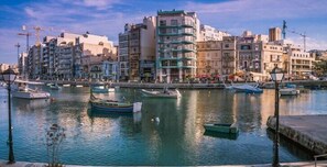 A marina with several boats docked, surrounded by multi-story buildings with balconies and various architectural styles. - Bookarest Hostel Malta (St. Julian's)