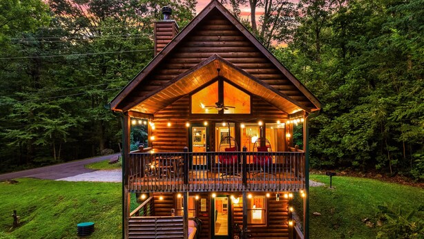 Una cabaña de troncos con balcón, zona de comedor y cocina a la vista.