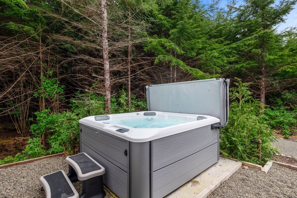 A hot tub in a forested area with a wooden deck and steps leading up to it.
